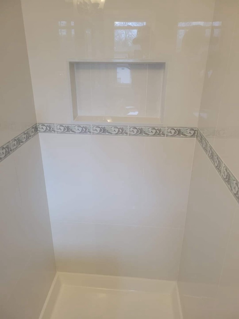 Finished white tile shower with decorative border and niche